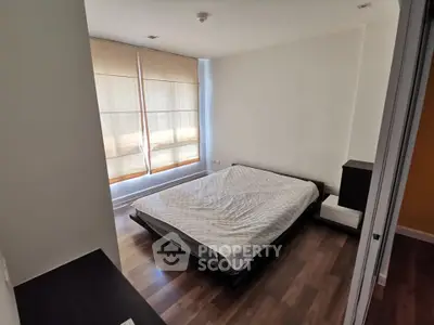 Modern minimalist bedroom with wooden flooring and large window for natural light.