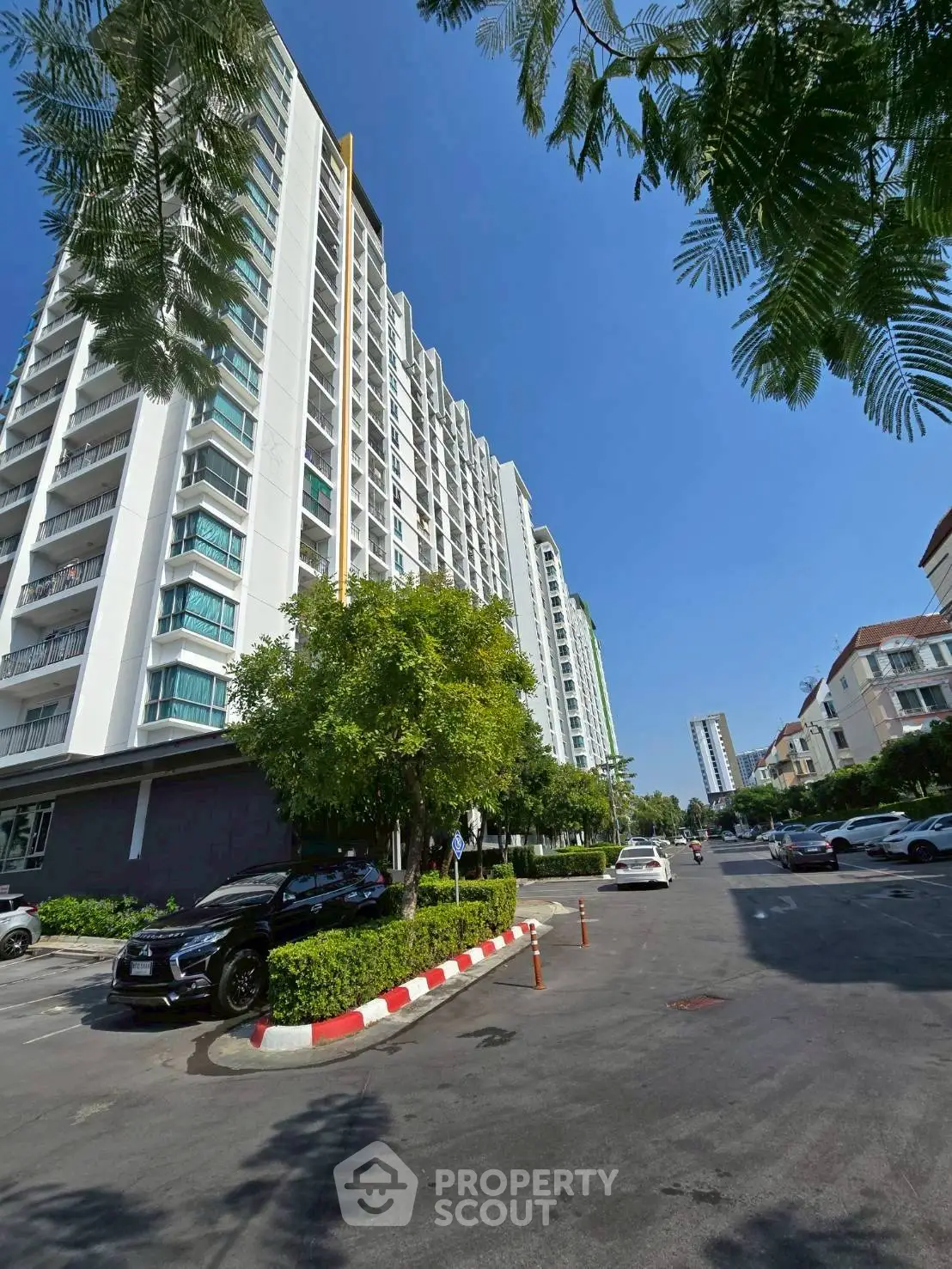 Modern high-rise apartment building with lush greenery and parking area