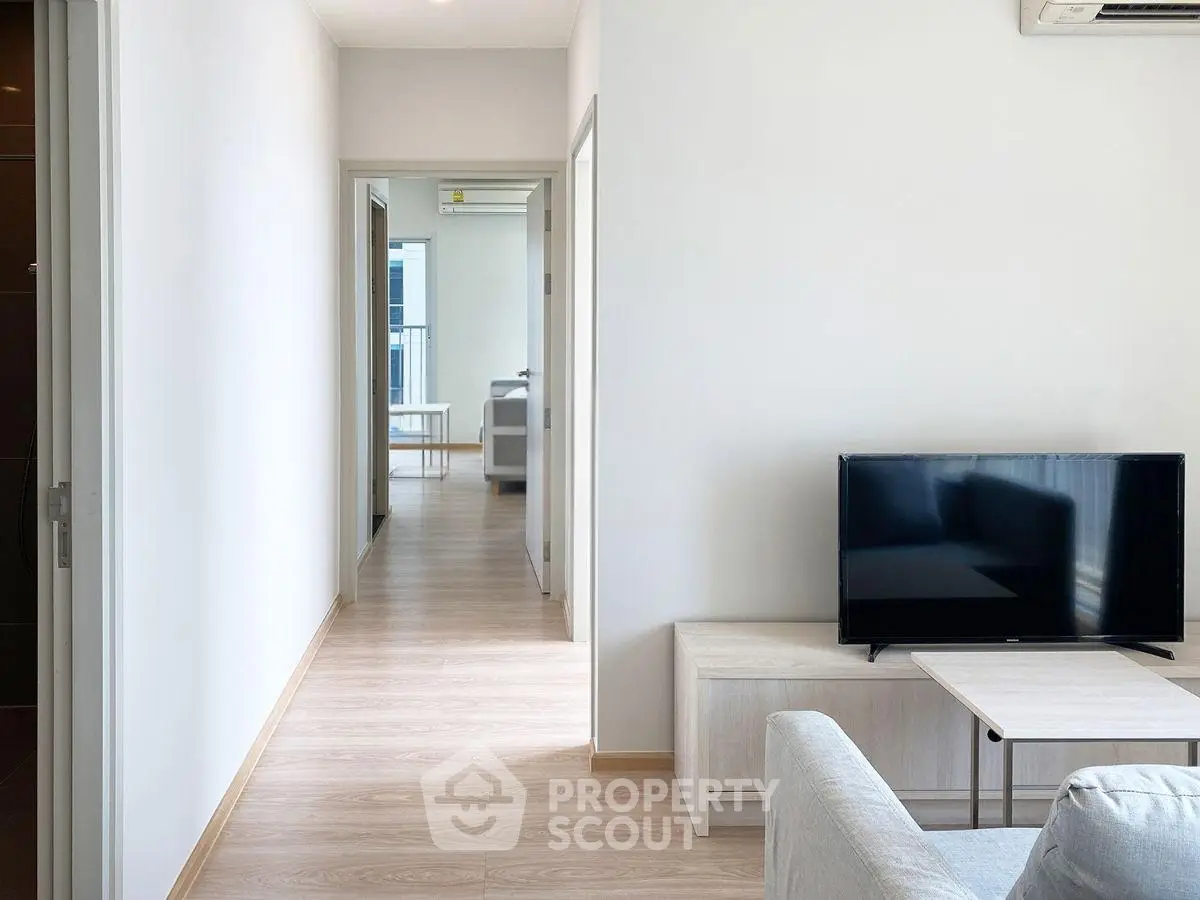 Modern apartment interior with sleek TV setup and bright hallway leading to rooms.