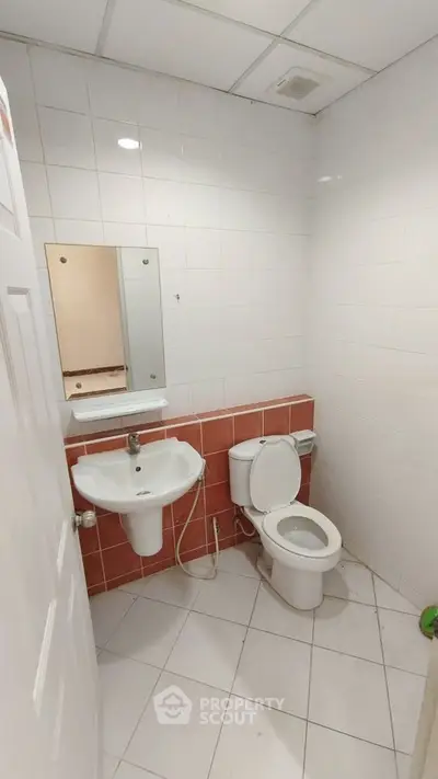 Compact bathroom with white tiles and red accents, featuring a sink and toilet.