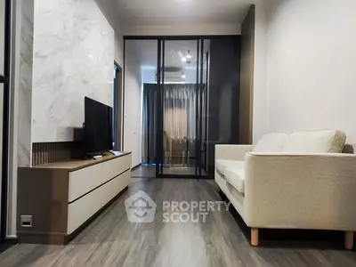 Modern living room with sleek design and glass partition, featuring a cozy sofa and flat-screen TV.