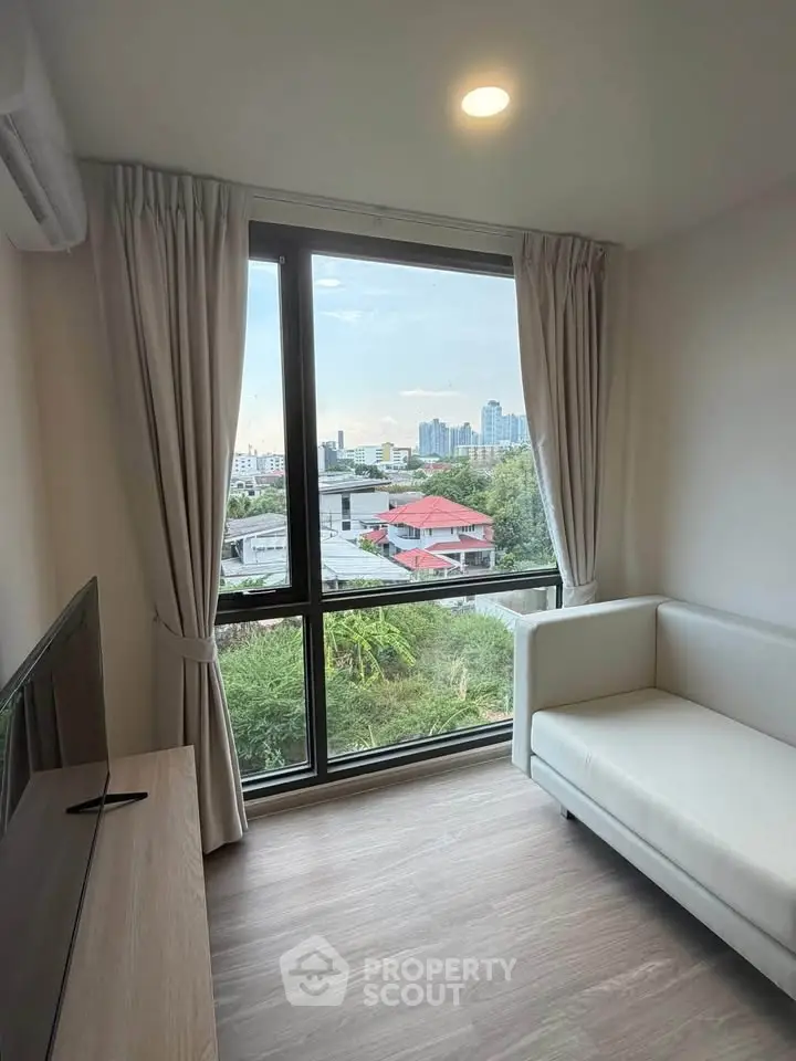 Bright living room with large window offering stunning city view, modern sofa, and sleek wooden flooring.
