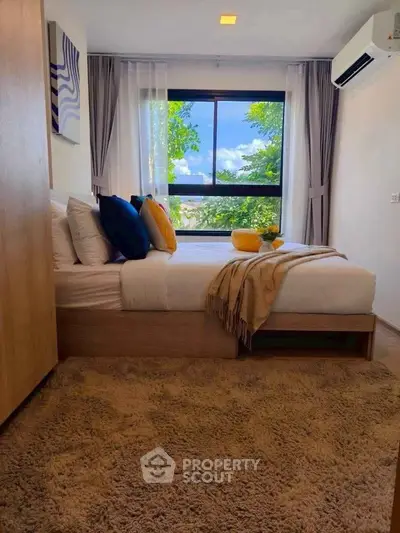 Cozy bedroom with large window and lush green view, featuring modern decor and plush carpeting.