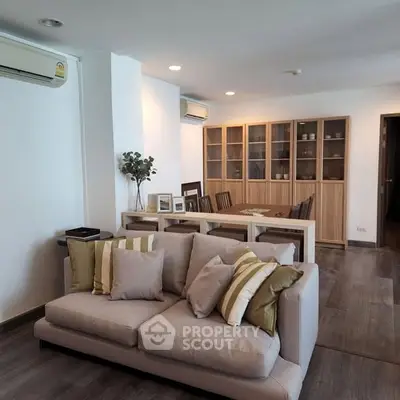 Spacious living room with modern decor and dining area, featuring elegant wooden flooring and stylish furniture.