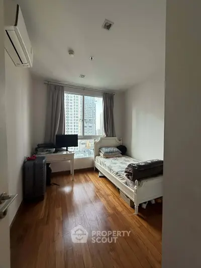 Cozy bedroom with wooden flooring and city view, featuring a single bed and desk setup.