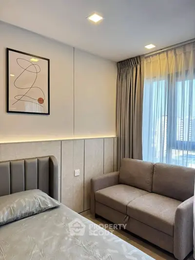 Modern bedroom with stylish decor and cozy seating area, featuring elegant lighting and large window.