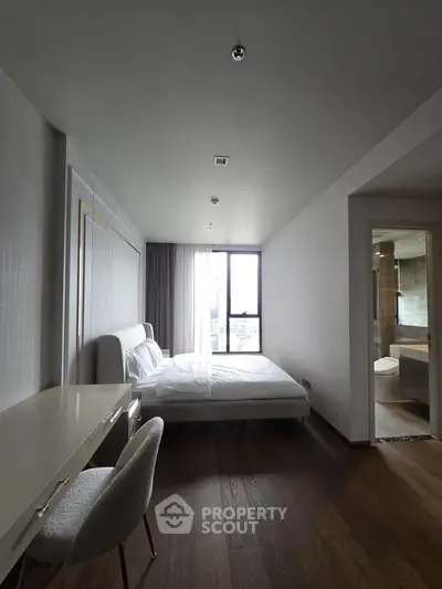 Modern bedroom with elegant decor and ensuite bathroom, featuring large window for natural light.