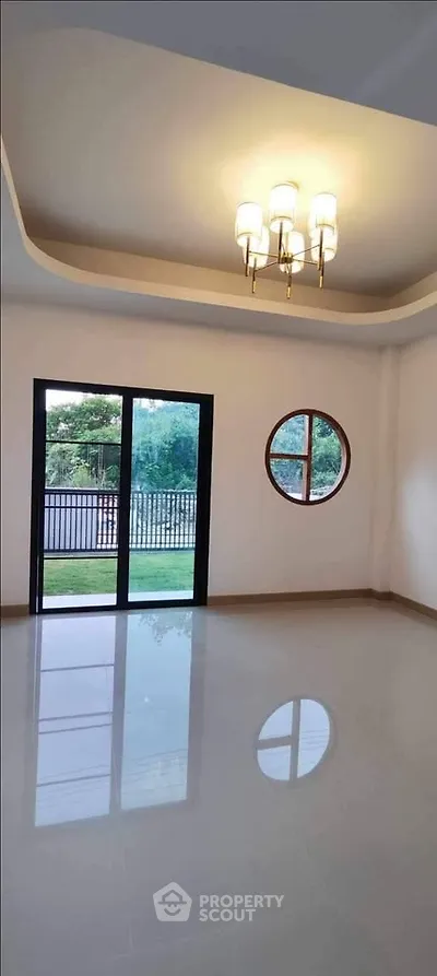 Spacious empty room with modern chandelier and large windows overlooking garden.
