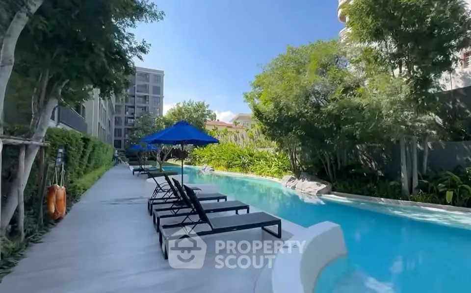 Luxurious poolside area with sun loungers and lush greenery in modern residential complex.