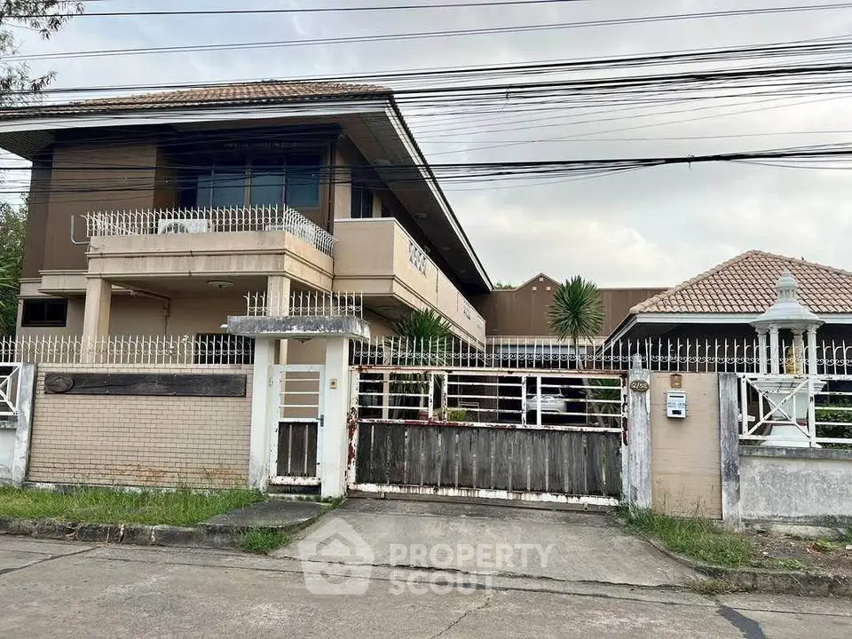 Spacious two-story house with gated entrance and lush greenery in a serene neighborhood.