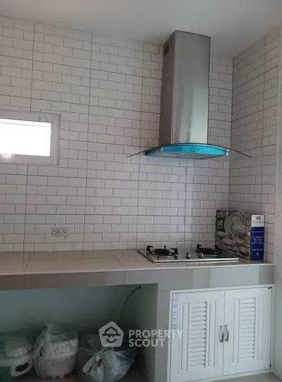 Modern kitchen with gas stove and sleek hood in a tiled setting.