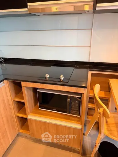 Modern kitchen with sleek black countertop and built-in microwave, featuring a stylish wooden chair.