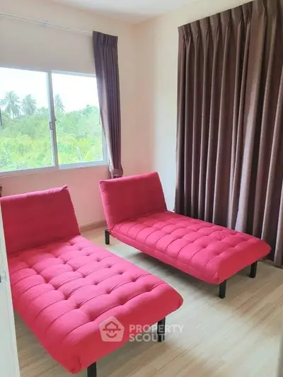 Bright room with two red chaise lounges and large window with lush green view.