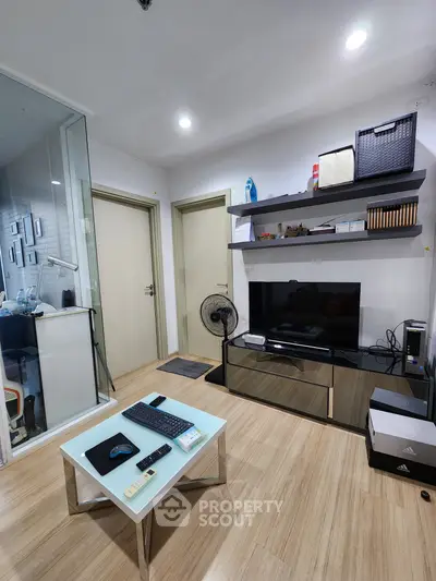 Modern living room with sleek design, featuring a TV, glass coffee table, and stylish shelving.