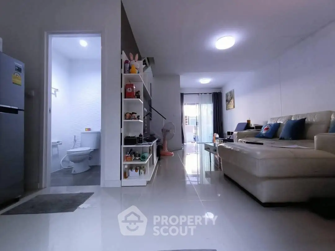 Modern living room with sleek white tiles and cozy beige sofa, open to a compact bathroom.