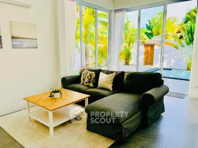 Bright living room with large windows overlooking tropical garden and pool, featuring a cozy sectional sofa.