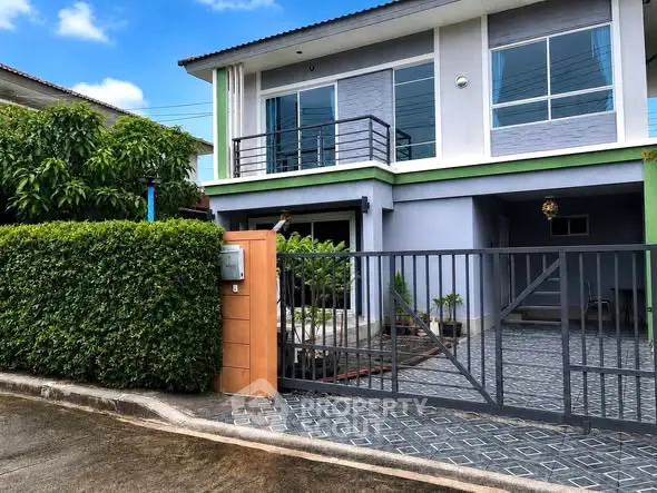Modern two-story house with gated driveway and lush greenery in suburban setting.