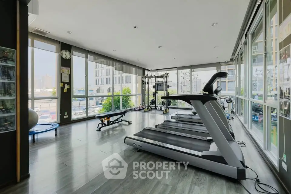 Spacious modern gym with large windows and city view, featuring treadmills and fitness equipment.