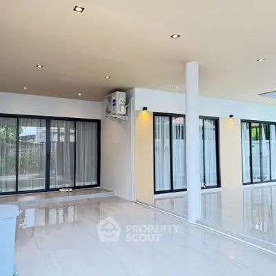 Spacious modern living area with large windows and sleek tile flooring, perfect for natural light and open space.