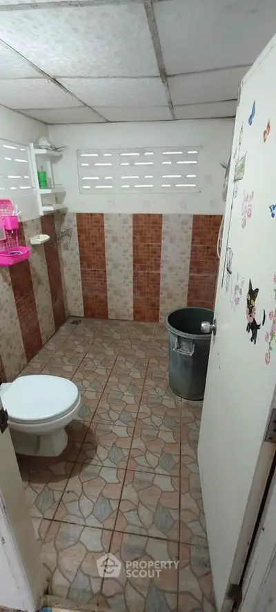 Cozy bathroom with tiled walls and floor, featuring a toilet and shower area.