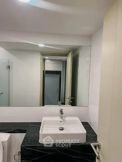 Modern bathroom with sleek sink and large mirror, featuring elegant black and white design.