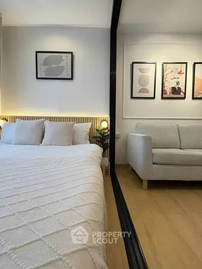 Modern bedroom with cozy bed and stylish sofa, featuring elegant wall art and warm lighting.
