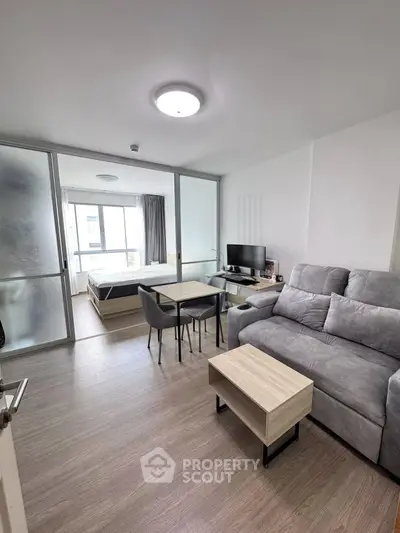 Modern studio apartment with cozy living area and bedroom separated by glass partition.