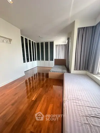 Spacious bedroom with wooden floors and large windows for natural light.