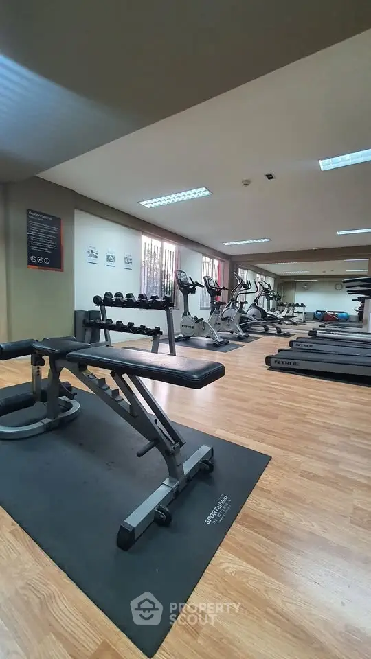 Spacious gym with modern equipment and wooden flooring in a residential building.