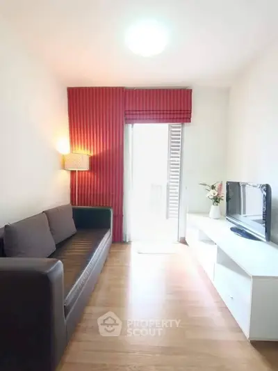 Cozy living room with modern sofa and TV unit, featuring red curtains and wooden flooring.
