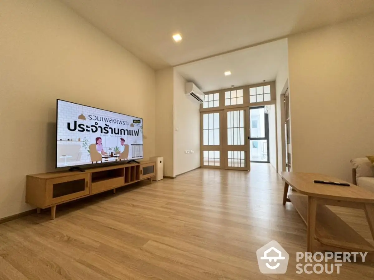 Spacious modern living room with wooden flooring and large TV, ideal for relaxation.