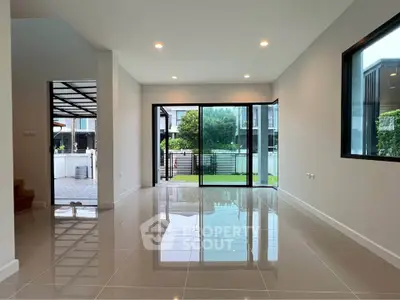 Spacious modern living room with large glass doors opening to a lush garden view.