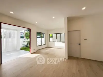 Spacious modern living room with large windows and wooden flooring, leading to a bright outdoor area.