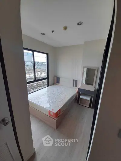Modern bedroom with large window and city view, featuring a bed and vanity set.