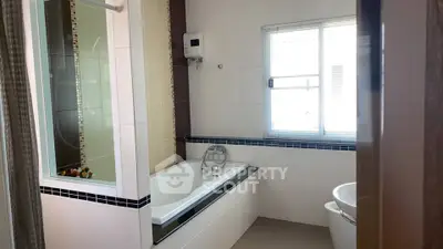 Modern bathroom with bathtub and natural light from window.