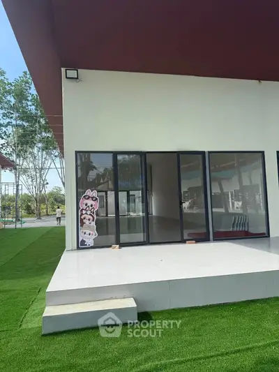 Modern building exterior with large glass doors and artificial grass lawn.