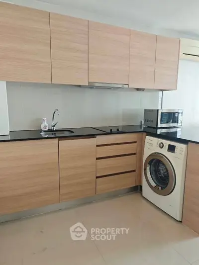 Modern kitchen with wooden cabinets, washing machine, and microwave in sleek apartment.