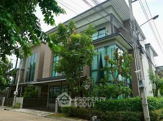 Modern multi-story house with large windows and lush greenery in a serene neighborhood.