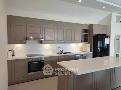 Modern kitchen with sleek cabinetry and island, featuring built-in oven and spacious fridge.