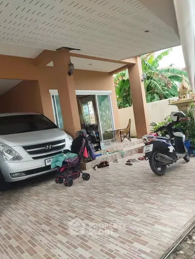 Spacious covered parking area with car and scooter, featuring tiled flooring and garden view.