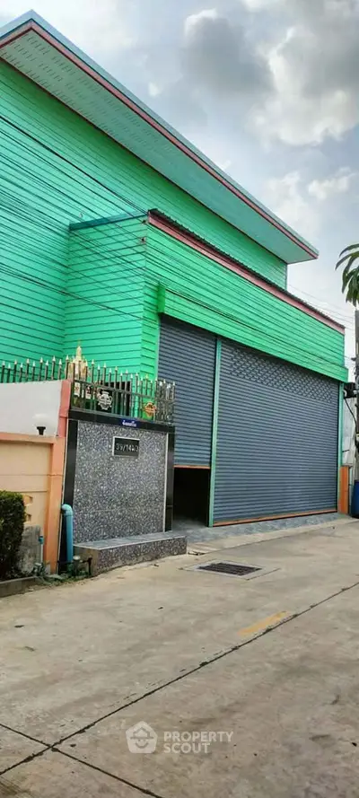 Vibrant green industrial building with large roller doors and secure gated entrance, perfect for commercial use.