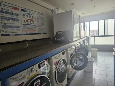 Modern laundry room with multiple washing machines and dryers in a bright apartment complex.