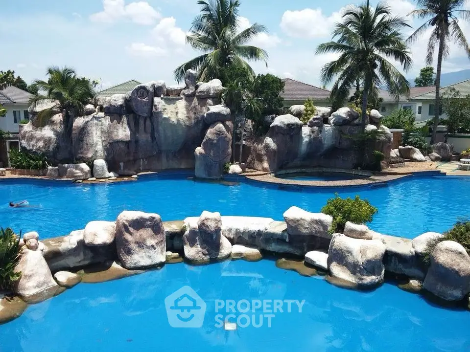 Luxurious resort-style pool with rock formations and palm trees in a serene residential area.