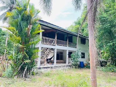 Charming two-story house surrounded by lush greenery, featuring a spacious balcony and rustic staircase.