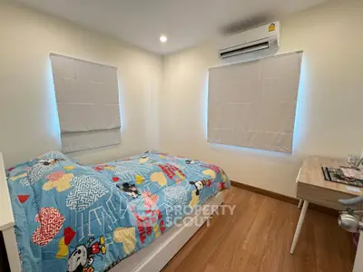 Cozy bedroom with wooden flooring and colorful bedding, featuring air conditioning and natural light.