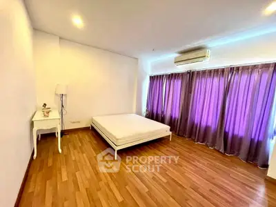 Spacious bedroom with wooden flooring and large windows with purple curtains.