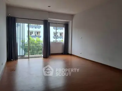 Spacious empty room with wooden flooring and large window overlooking balcony.