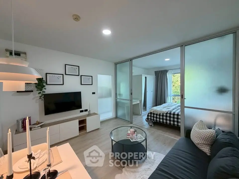 Modern open-plan living room with glass partition leading to cozy bedroom, stylish decor, and natural light.