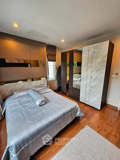 Modern bedroom with stylish decor and wooden flooring, featuring a cozy bed and mirrored wardrobe.