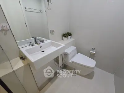 Modern bathroom with sleek fixtures and minimalist design, featuring a white sink and toilet.